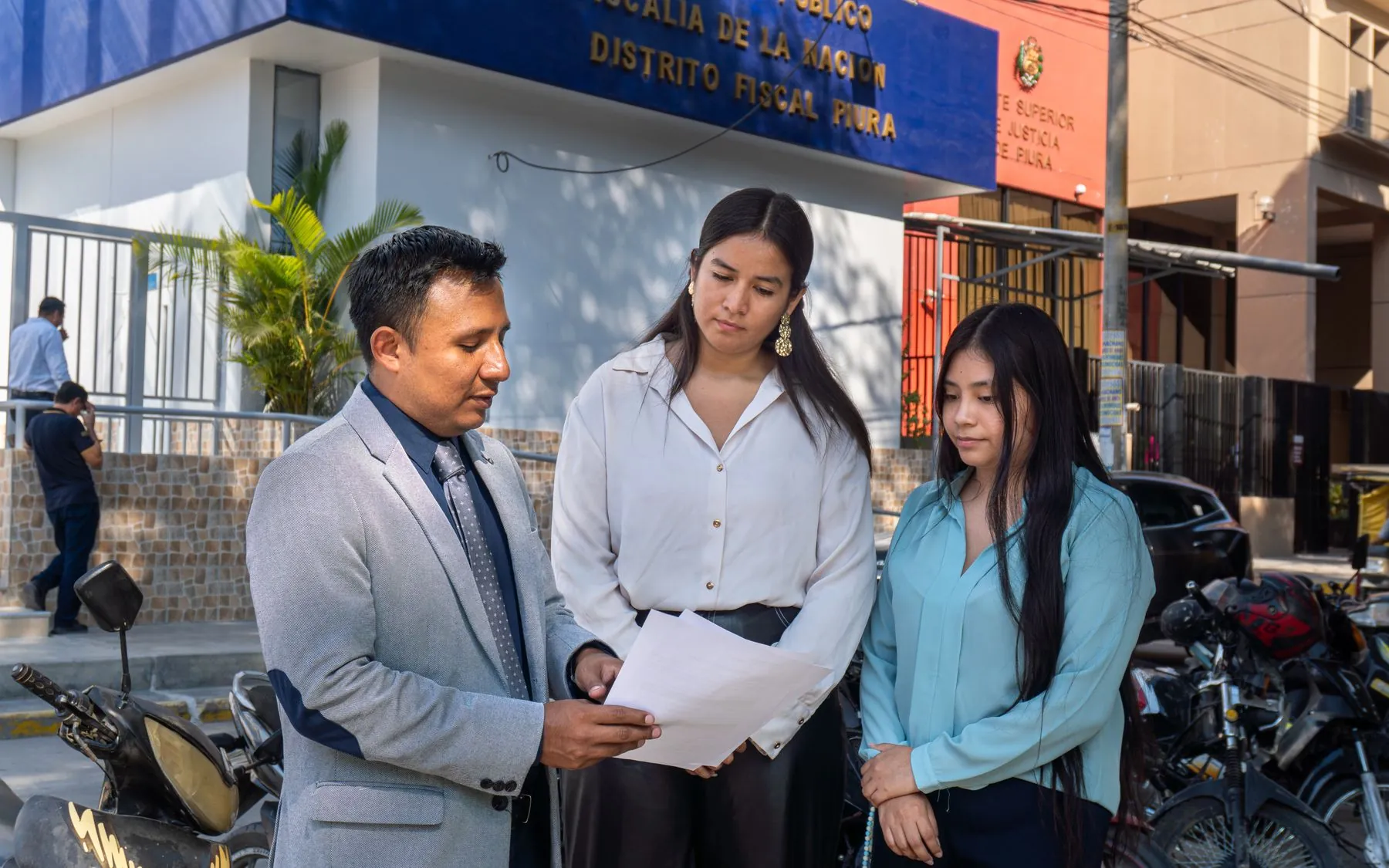 Dos mujeres revisan un documento con un asesor frente a una oficina en Piura